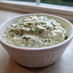 Close-up of a creamy, white dill dip generously mixed with fresh green dill, served in a small white bowl.