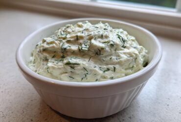 Close-up of a creamy, white dill dip generously mixed with fresh green dill, served in a small white bowl.