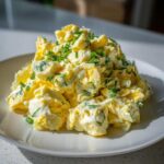 A generous serving of creamy egg salad recipe, featuring chopped eggs and topped with bright green chives.