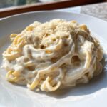 Close-up of fettuccine pasta generously coated in creamy homemade alfredo sauce and topped with grated Parmesan cheese.