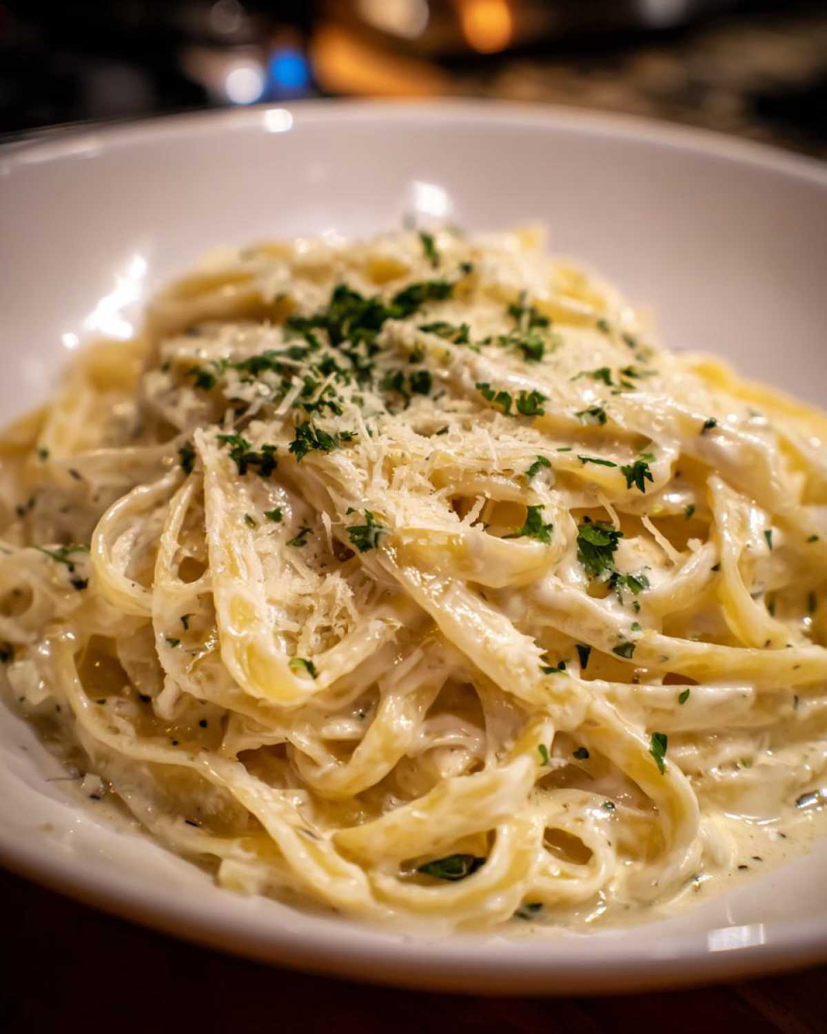 Close-up of fettuccine pasta coated in creamy Olive Garden Alfredo Sauce, topped with Parmesan cheese and parsley.