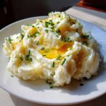 A close-up of fluffy garlic mashed potatoes topped with melted butter and fresh chopped chives.