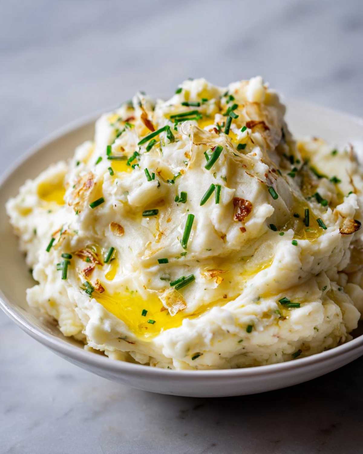 Close-up of fluffy garlic mashed potatoes topped with melted butter, chopped chives, and crispy garlic pieces.