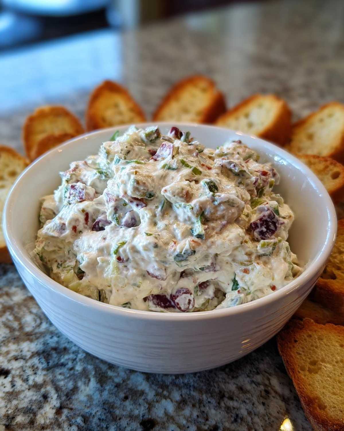 A white bowl filled with creamy, chunky hoagie dip surrounded by toasted bread slices.