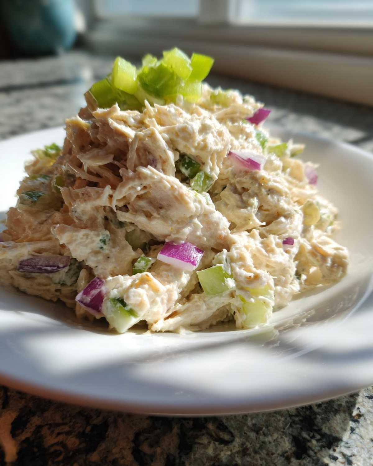 A mound of creamy honey mustard chicken salad mixed with diced red onion and celery, garnished with green onion.