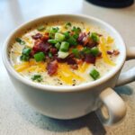 A close-up of creamy loaded baked potato soup topped with cheddar cheese, bacon bits, and fresh green onions.