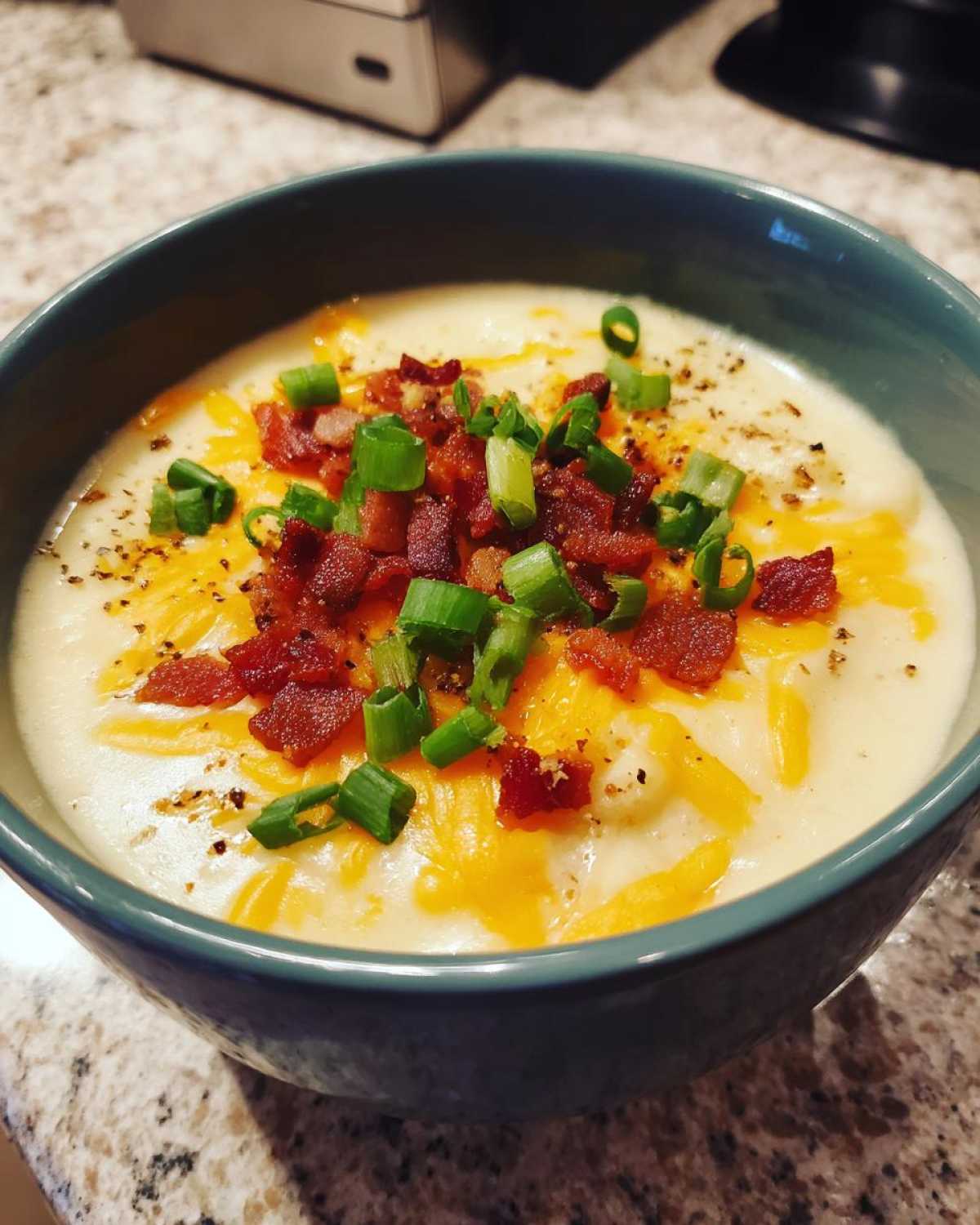 A close-up of a bowl of creamy loaded baked potato soup topped with shredded cheese, bacon bits, and green onions.