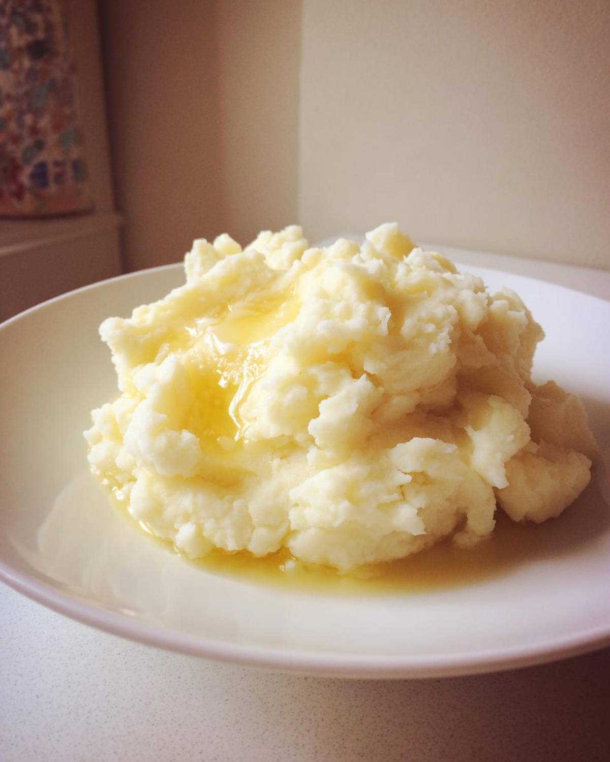 A generous serving of fluffy, creamy mashed potatoes topped with melted butter pooling slightly on the white plate.