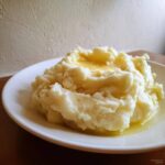 A generous serving of fluffy, creamy mashed potatoes topped with a pool of melted butter on a white plate.
