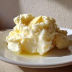 A generous serving of fluffy, creamy mashed potatoes topped with a pat of melting butter on a white plate.
