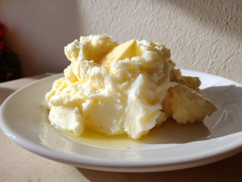 A generous serving of fluffy, creamy mashed potatoes topped with a pat of melting butter on a white plate.