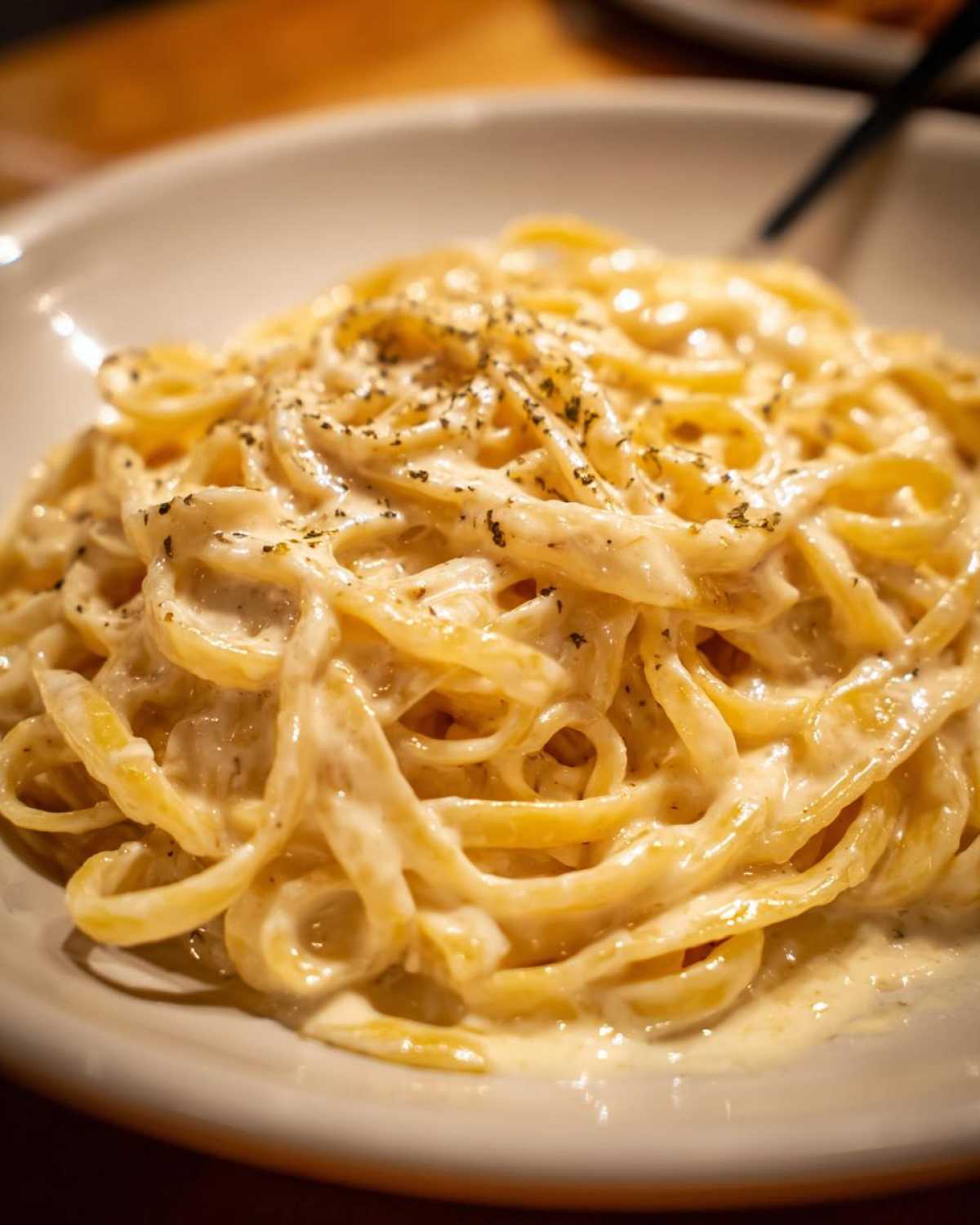 Close-up of fettuccine pasta generously coated in rich, creamy Olive Garden Alfredo Sauce and sprinkled with herbs.