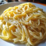 Close-up of fettuccine pasta generously coated in creamy Olive Garden Alfredo sauce and sprinkled with pepper.