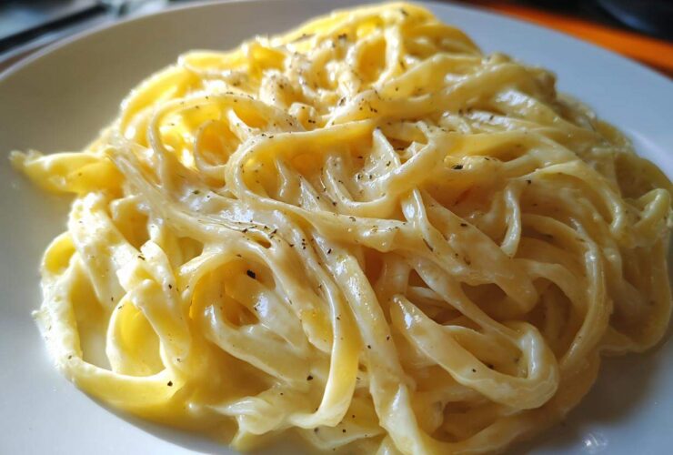 Close-up of fettuccine pasta generously coated in creamy Olive Garden Alfredo sauce and sprinkled with pepper.