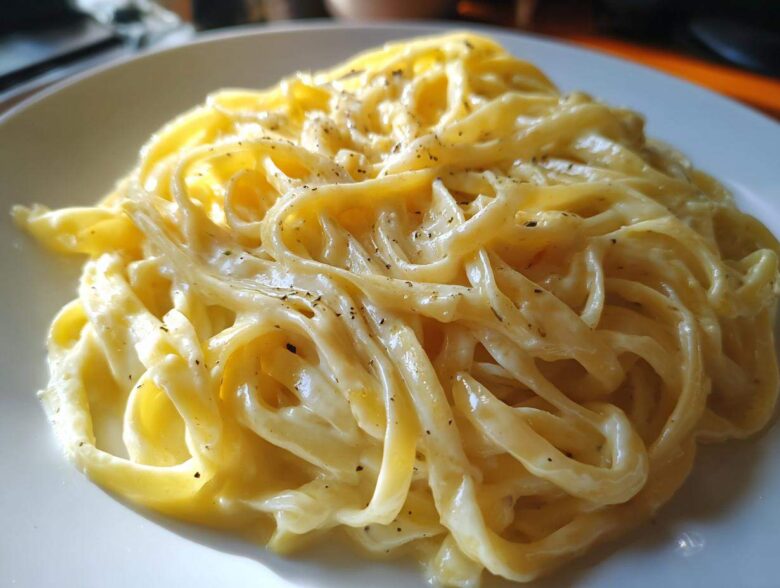 Close-up of fettuccine pasta generously coated in creamy Olive Garden Alfredo sauce and sprinkled with pepper.