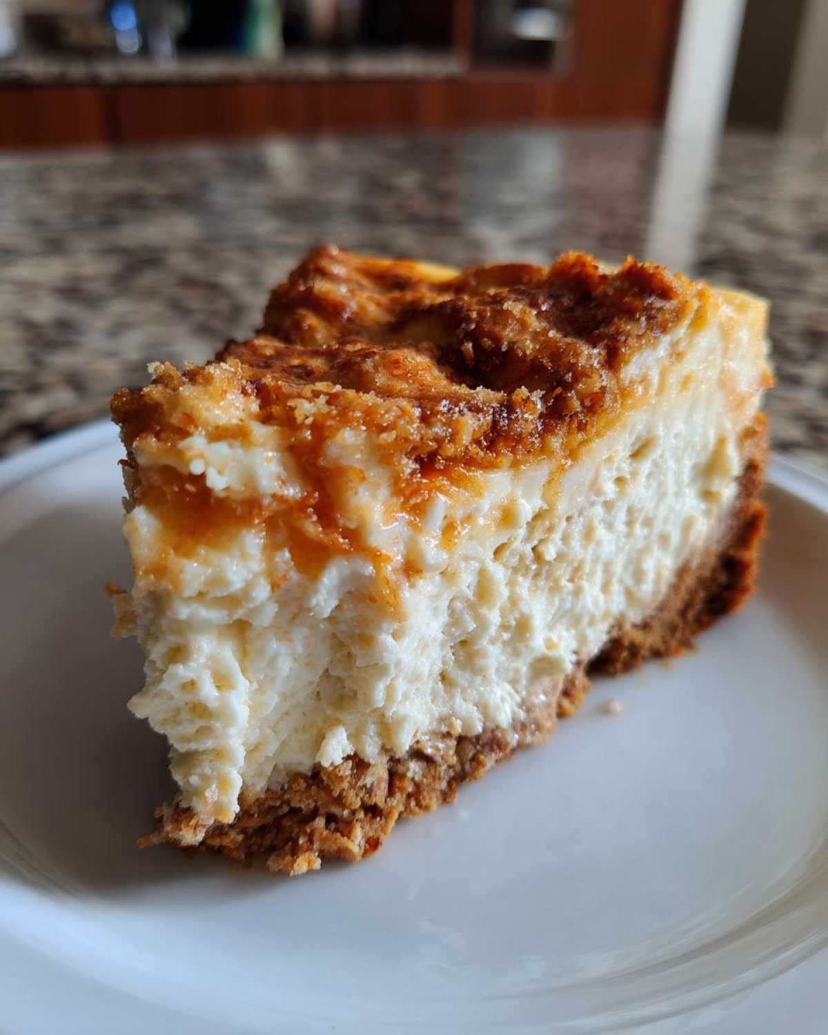 Close-up of a thick, creamy slice of Protein Cheesecake on a white plate, featuring a graham cracker crust and caramelized topping.