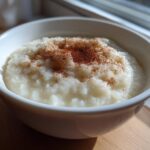 Close-up of a white bowl filled with creamy rice pudding, topped generously with ground cinnamon.