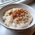 Close-up of creamy rice pudding in a white bowl, generously topped with ground cinnamon.
