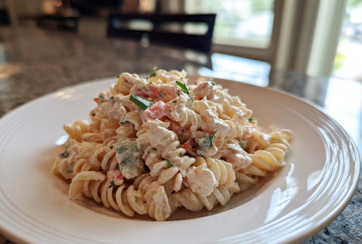 A close-up of a serving of creamy tuna pasta salad mixed with rotini pasta and chopped vegetables on a white plate.