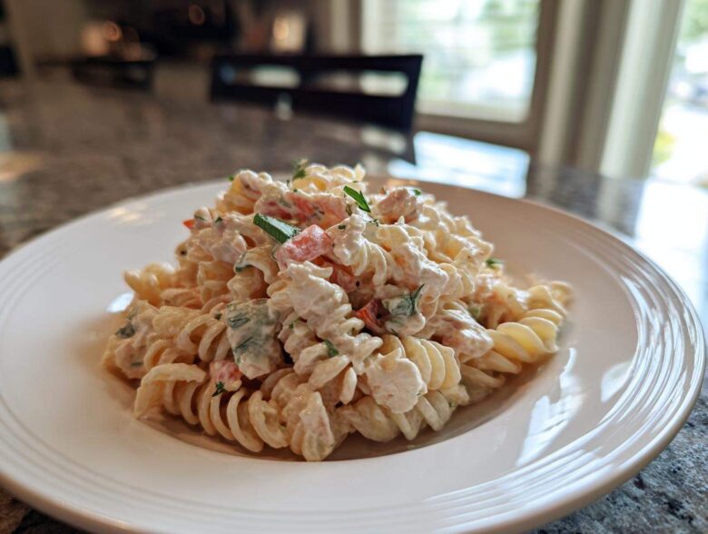 A close-up of a serving of creamy tuna pasta salad mixed with rotini pasta and chopped vegetables on a white plate.