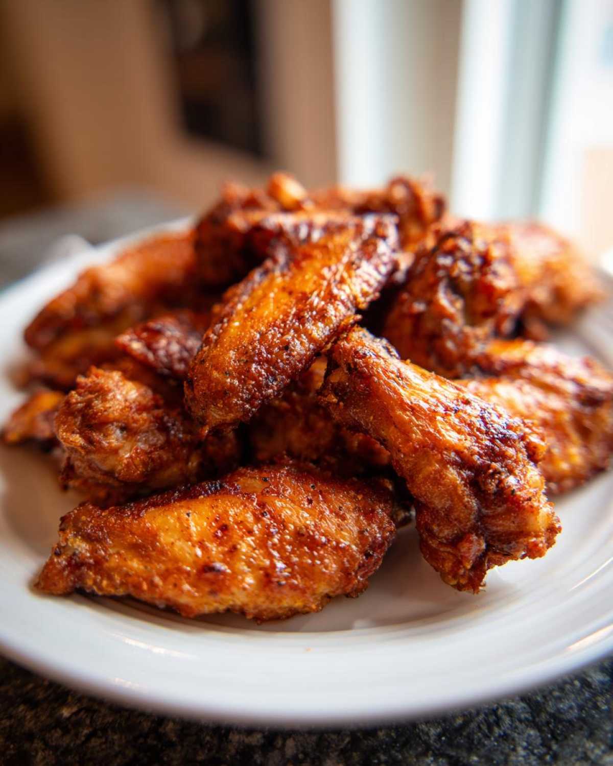 A close-up of a pile of golden brown and crispy baked chicken wings served on a white plate.