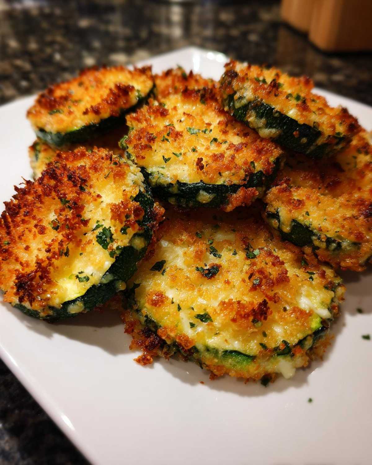 A close-up of golden brown, crispy baked parmesan zucchini slices piled on a white plate.