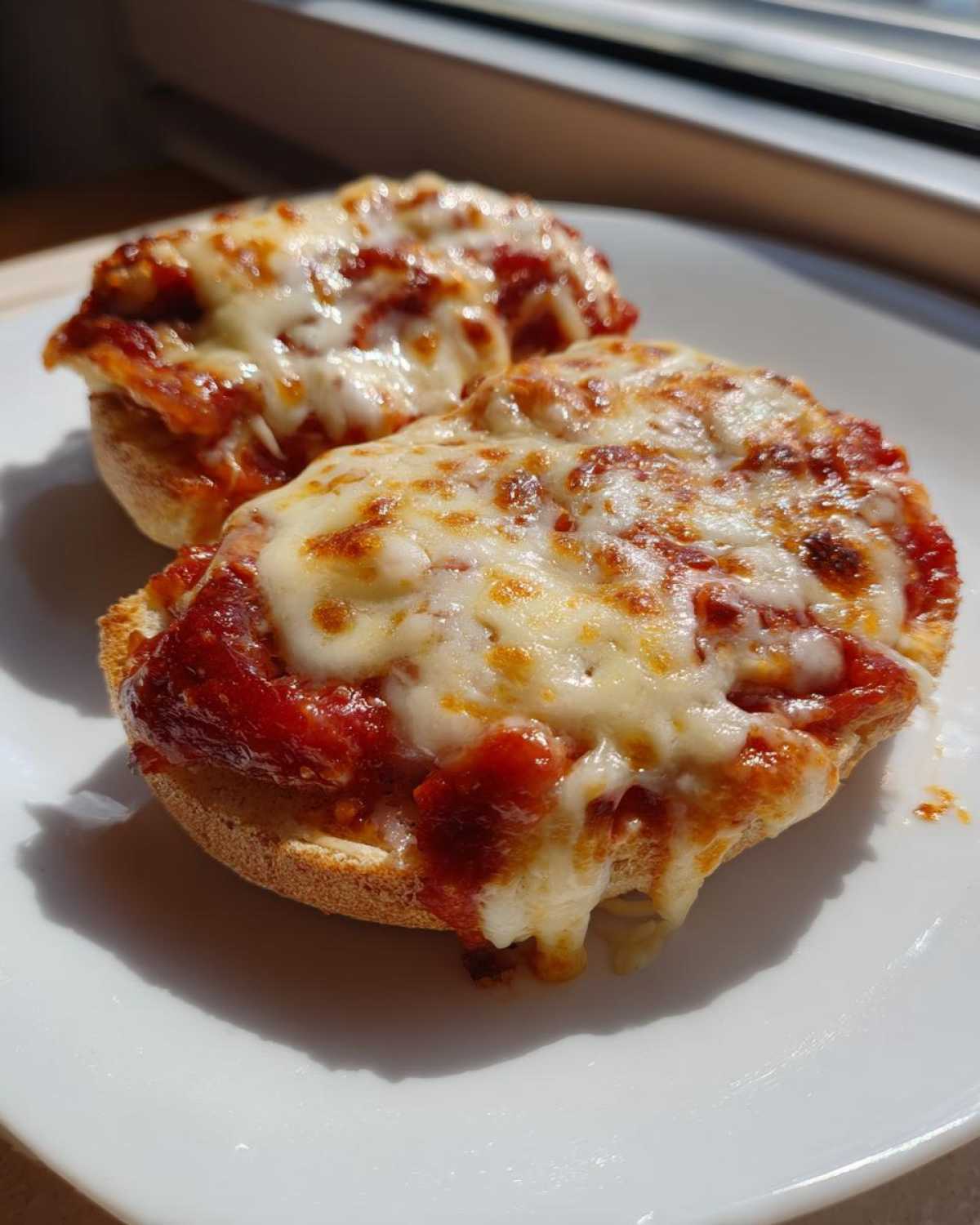 Two halves of a crispy english muffin pizza topped with rich tomato sauce and bubbly, melted mozzarella cheese.