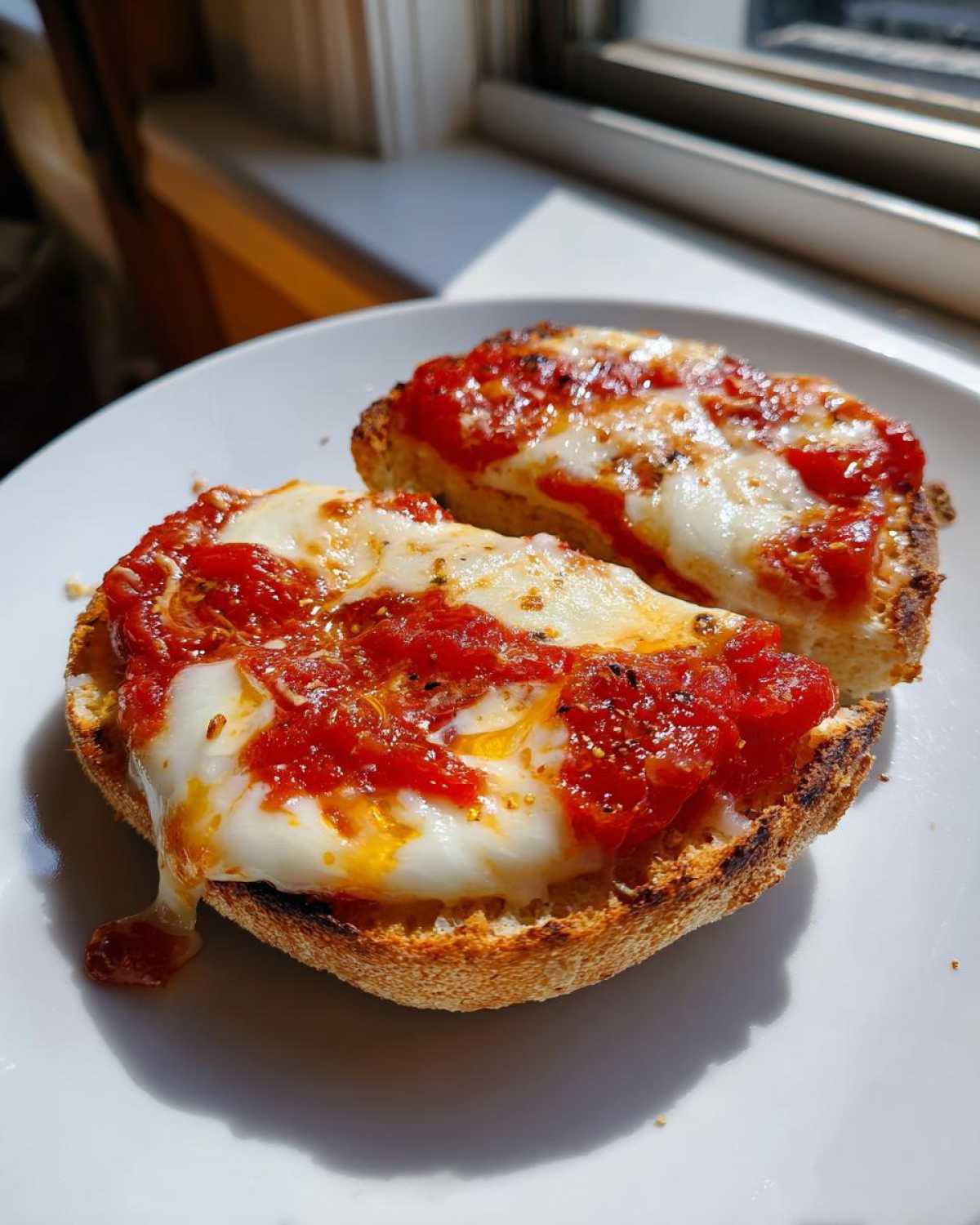 Two halves of a crispy English muffin pizza topped with bright red sauce and gooey melted mozzarella cheese.