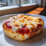 Close-up of a perfectly toasted English muffin pizza topped with bubbling tomato sauce and melted mozzarella cheese.