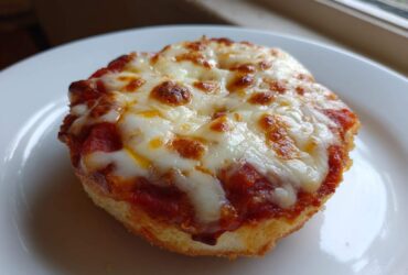 A close-up of a single, crispy english muffin pizza topped with bubbling tomato sauce and melted, slightly browned mozzarella cheese.