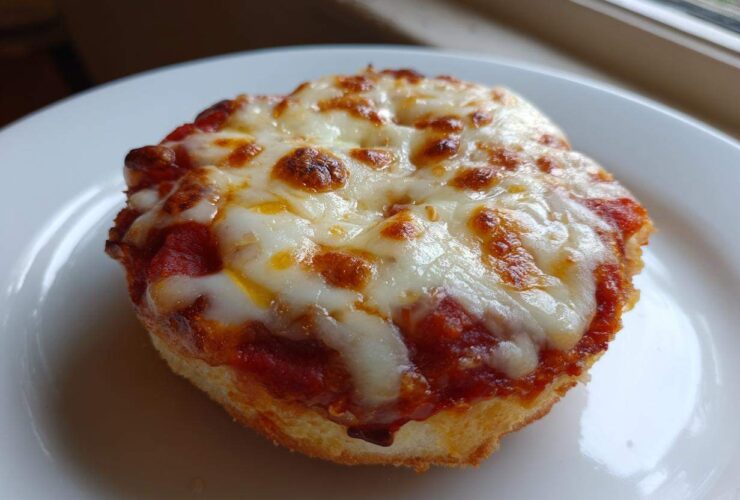 A close-up of a single, crispy english muffin pizza topped with bubbling tomato sauce and melted, slightly browned mozzarella cheese.