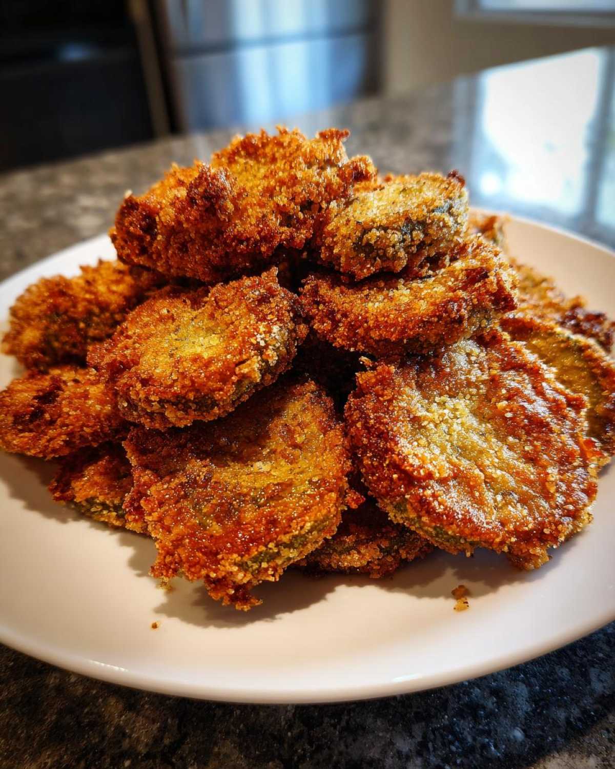 A tall pile of golden brown, crispy Fried Pickles served on a white plate.