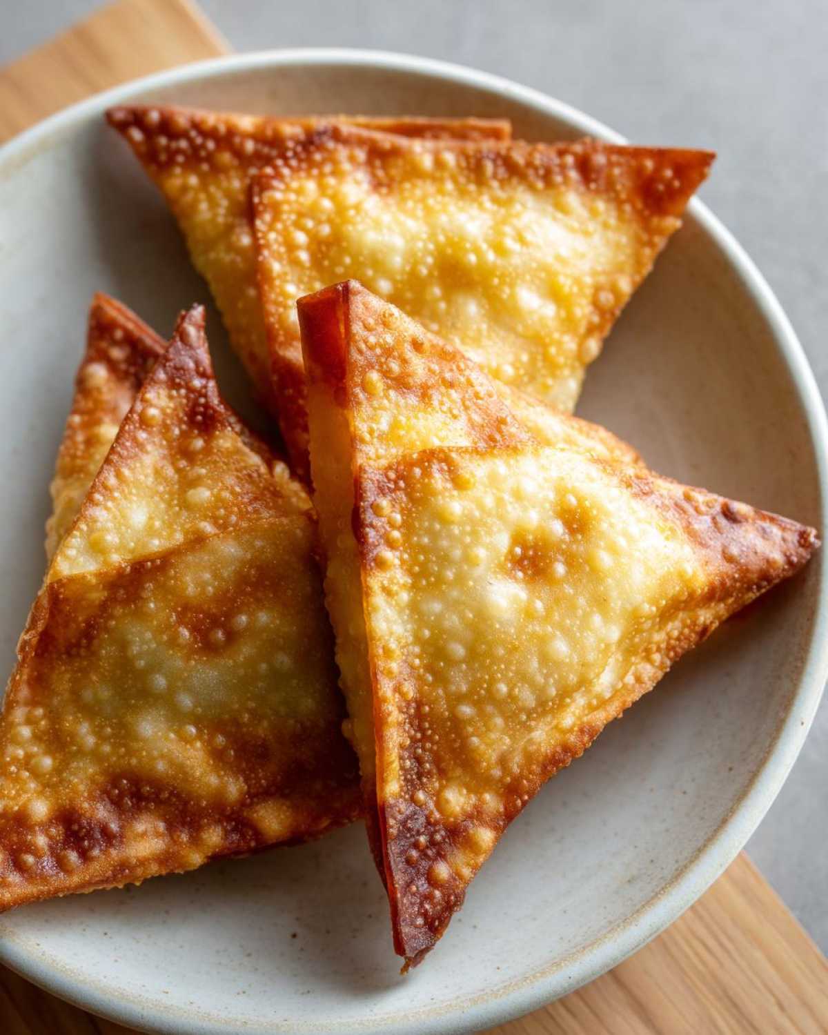 Close-up of four golden-brown, crispy fried wonton triangles, similar to a low-calorie egg roll, served in a light ceramic bowl.