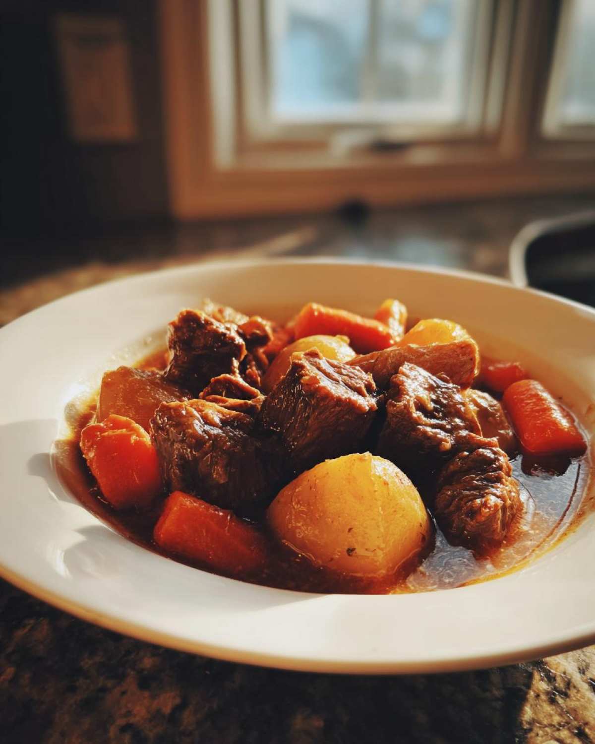 A close-up of a white bowl filled with rich, dark crockpot beef stew featuring tender beef chunks, potatoes, and carrots.