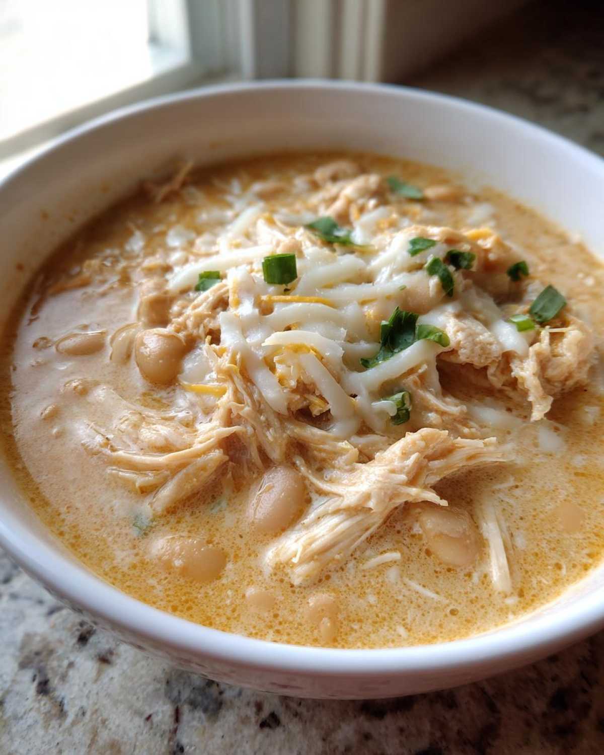 Close-up of a bowl of creamy crockpot white chicken chili topped with shredded cheese and green onions.