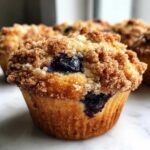 A close-up of a golden brown blueberry muffin topped with crunchy brown sugar streusel.