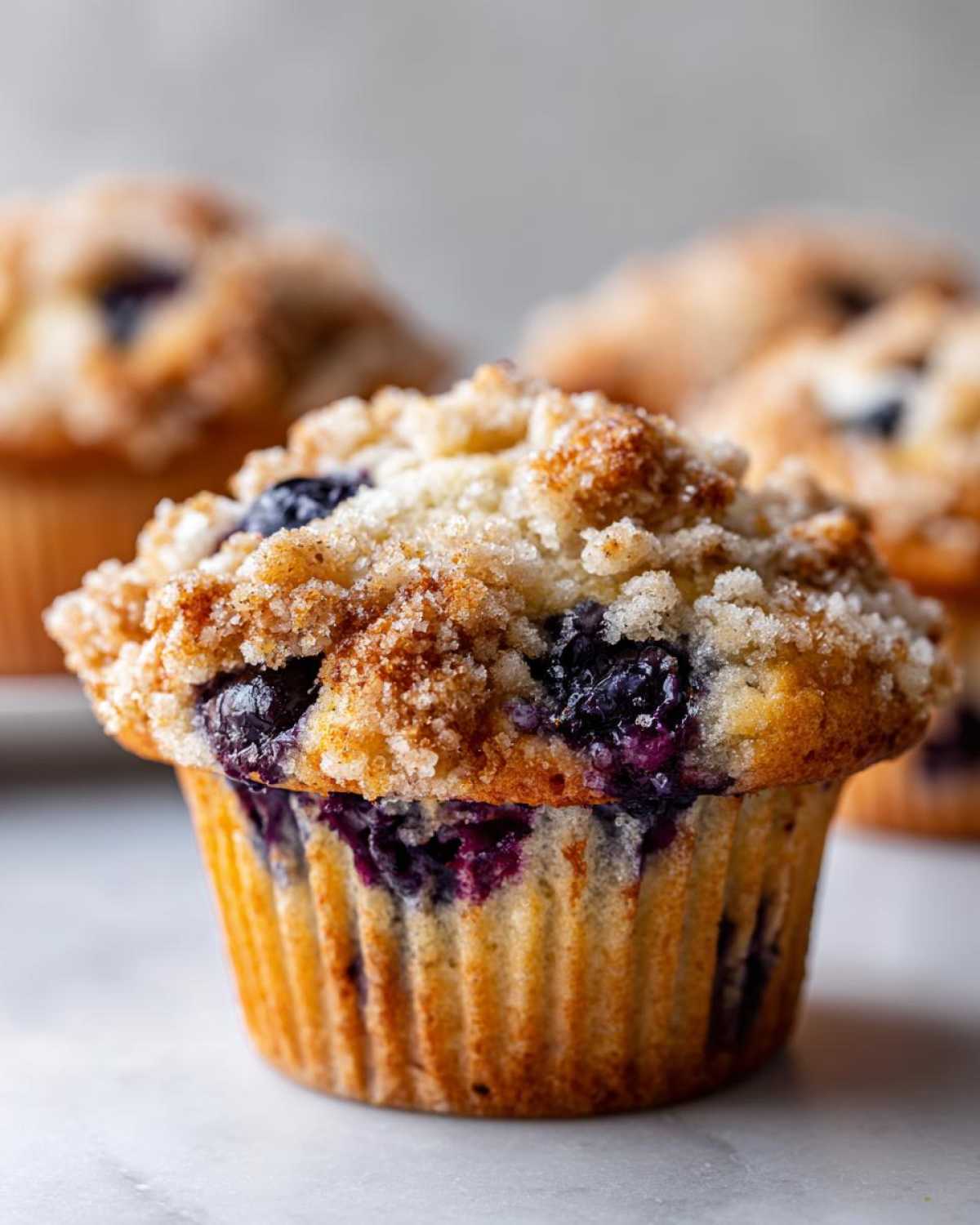 A close-up of a golden baked blueberry muffin topped with a generous cinnamon sugar crumb topping.