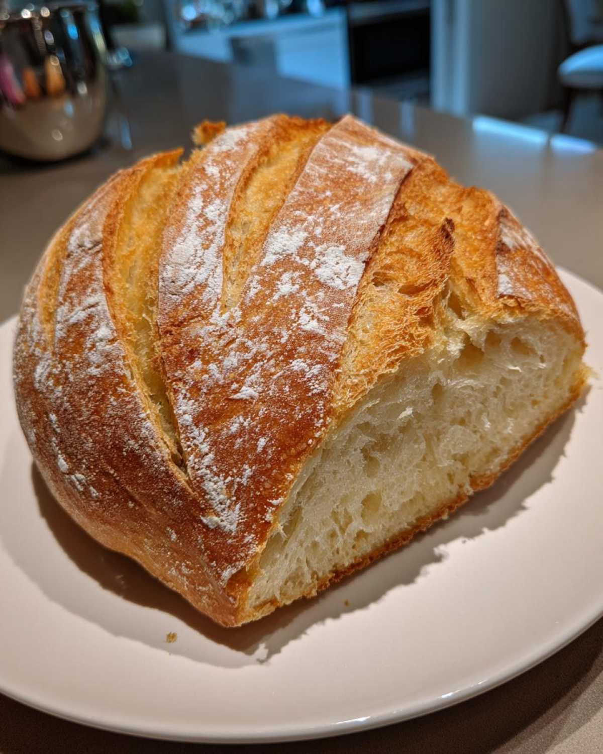 A freshly baked loaf of French bread, sliced open to show the soft interior and golden, scored crust dusted with flour.