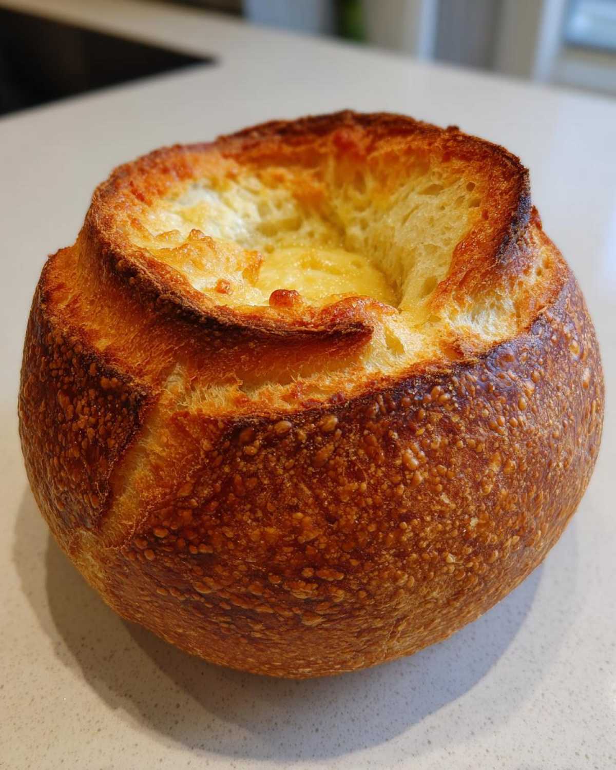 Close-up of a golden brown, crusty round bread bowl ready to be filled, showcasing the hollowed-out center.