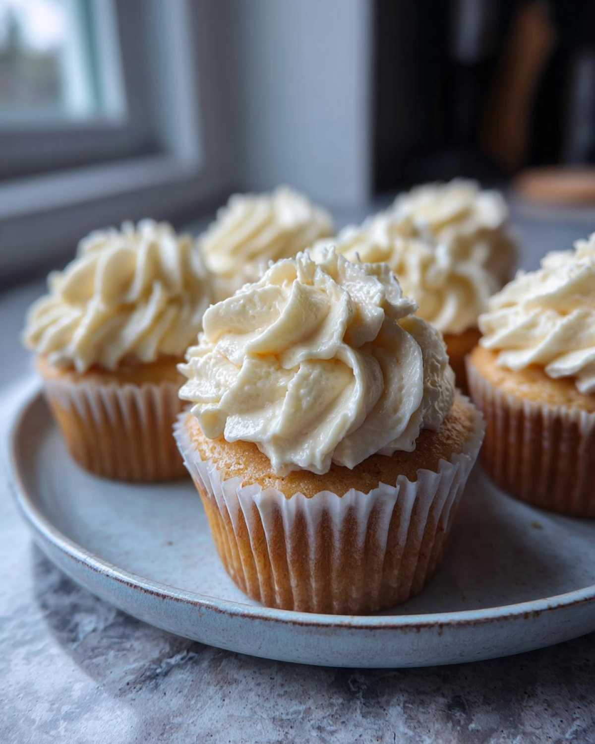 Close-up of vanilla cupcakes topped high with swirls of creamy vanilla buttercream frosting.