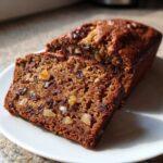 Close-up of a freshly baked date nut bread loaf, sliced to show moist interior with visible dates and walnuts.