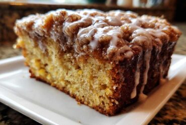 Close-up of a moist slice of coffee cake topped with cinnamon streusel and drizzled with vanilla glaze.
