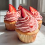 Close-up of several divine strawberry cupcakes topped with pink strawberry frosting and a fresh strawberry slice.