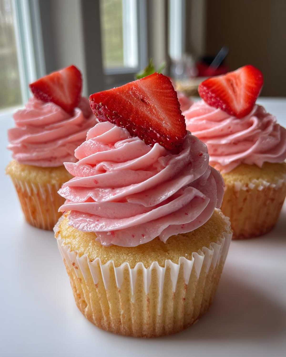 Three perfectly frosted strawberry cupcakes topped with fresh strawberry slices, showcasing the pink strawberry frosting.