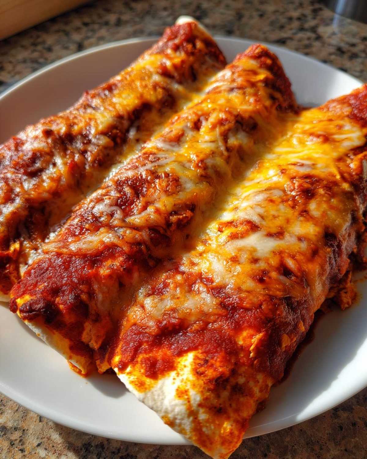 Close-up of three baked easy chicken enchiladas covered in rich red sauce and melted orange and white cheese.