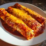 Three rolled easy chicken enchiladas covered in red sauce and melted cheddar cheese on a white plate.