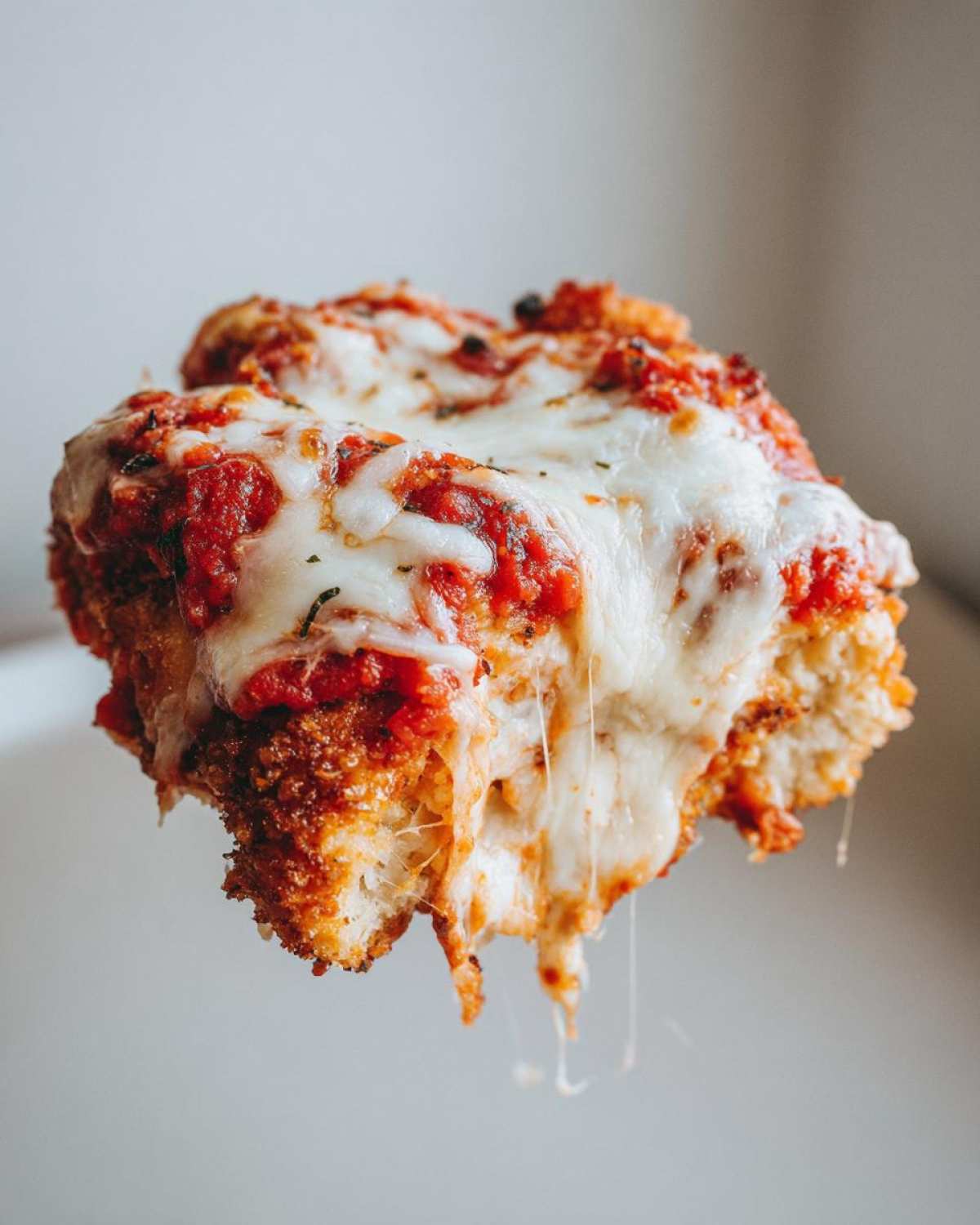 Close-up of a serving of Easy Chicken Parmesan being lifted, showing melted, stringy mozzarella cheese and rich tomato sauce.