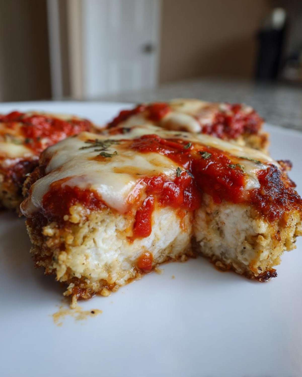 Close-up of Easy Chicken Parmesan cut open showing white chicken breast, crispy breading, marinara sauce, and melted mozzarella cheese.