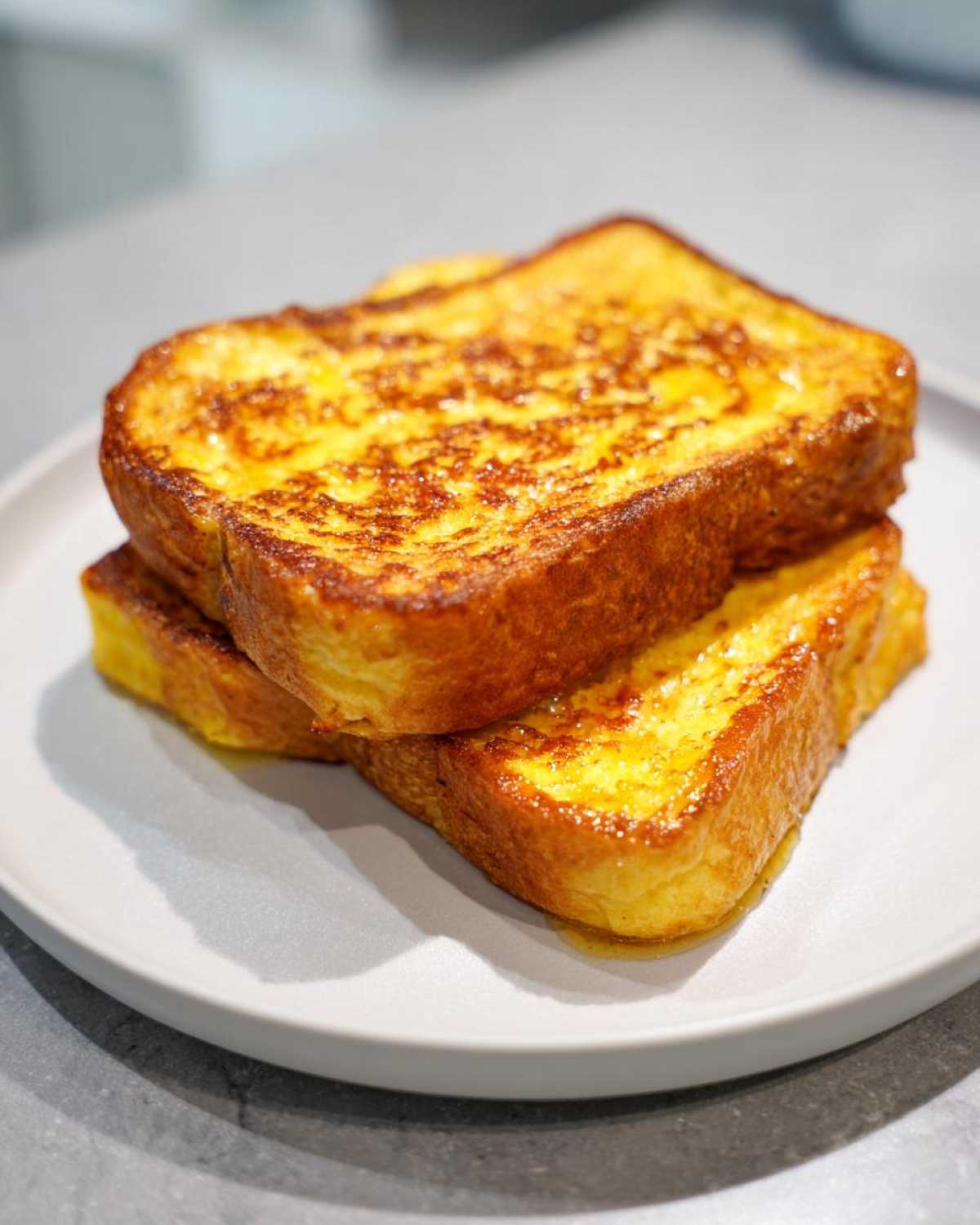 Two golden brown slices of easy french toast stacked on a light grey plate, glistening with syrup.