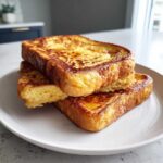 A stack of three thick, golden-brown slices of easy french toast served on a white plate.